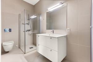 Badet er innredet med vegghengt toalett, servant nedfelt i innredning, dusjhjørne med svingbare glassdører og opplegg for vaskemaskin