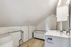 Badet er innredet med dusj i badekar, et toalett, hvit servantinnredning og en varmtvannsbereder fra 2014.
