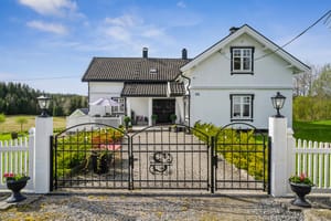 Våningshuset har pent opparbeidet hage og uteareal, avgrenset av hvitmalt gjerde og flotte smijernsporter mot tunet.