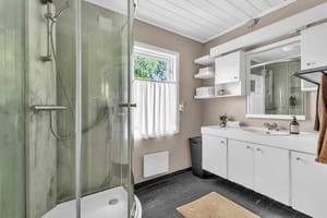 Badet har lysmalte vegger og grå gulvfliser, og varmekilden i rommet er panelovn. Godt med oppbevaring i vegg- og servantskap