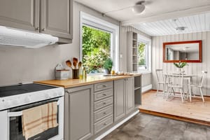 Innredningen har lysegrå, profilerte fronter, vitrinedører, takhøye skap og lys laminatbenkeplate med nedfelt kum i stål