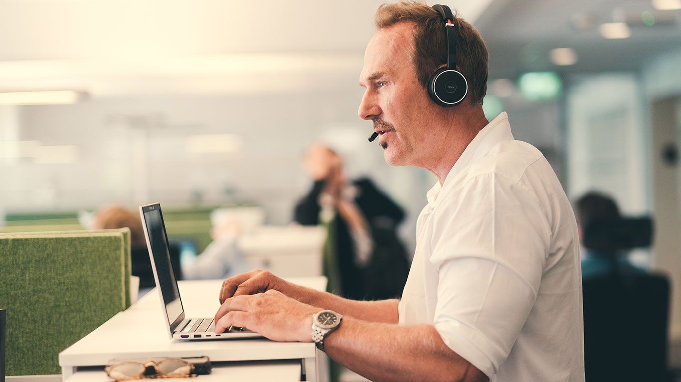 Mann arbeider ved PC, snakker i headset på telefonen