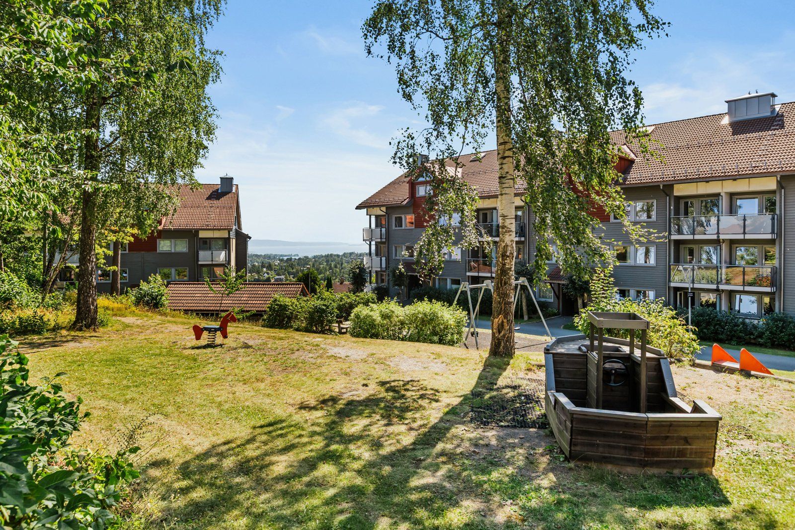 Pent opparbeidet fellesområde med gressplen- og grøntområder, beplantning, lekeplass og sittegrupper