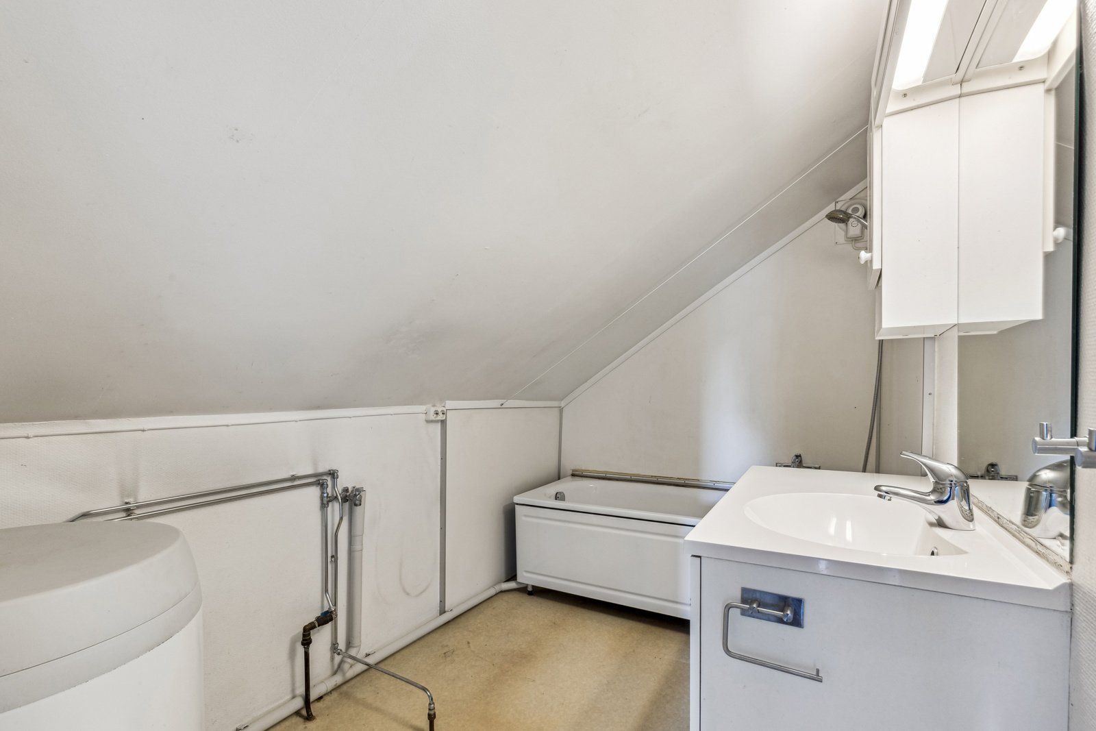 Badet er innredet med dusj i badekar, et toalett, hvit servantinnredning og en varmtvannsbereder fra 2014.
