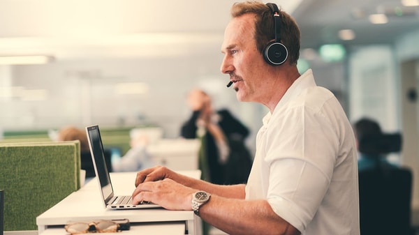 Mann arbeider ved PC, snakker i headset på telefonen
