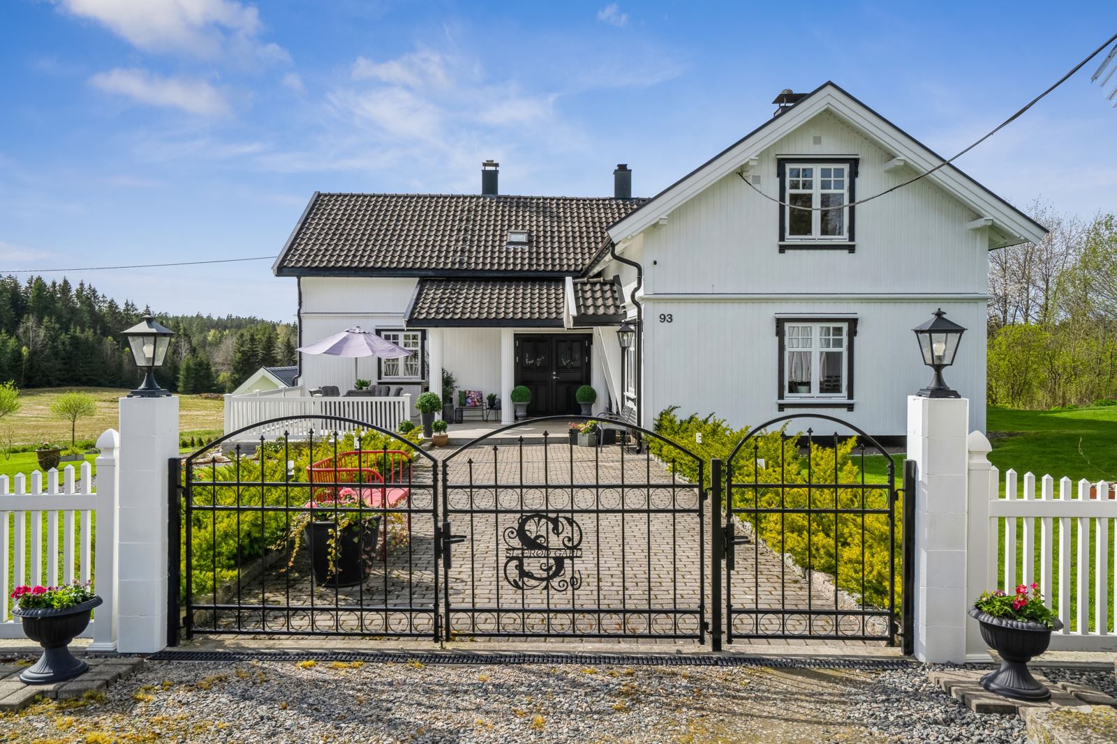 Våningshuset har pent opparbeidet hage og uteareal, avgrenset av hvitmalt gjerde og flotte smijernsporter mot tunet.